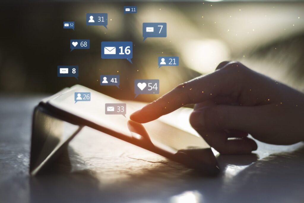 A close-up of a finger tapping a tablet screen with floating digital notification icons for messages, likes, and followers.